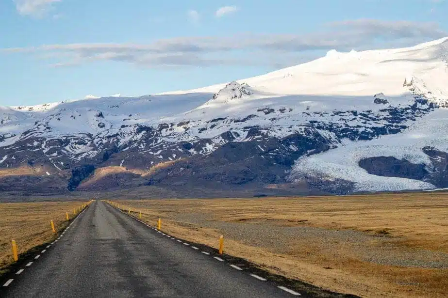 Cosas únicas para hacer alrededor de Vik, largo camino a través de pastizales marrones que conducen a grandes montañas cubiertas de nieve bajo un cielo azul nublado
