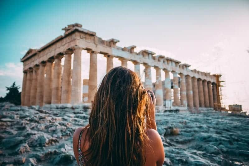 Atenas a Saranda, Albania / Saranda a Atenas, Grecia, persona frente al Partenón con cámara en la luz del amanecer temprano