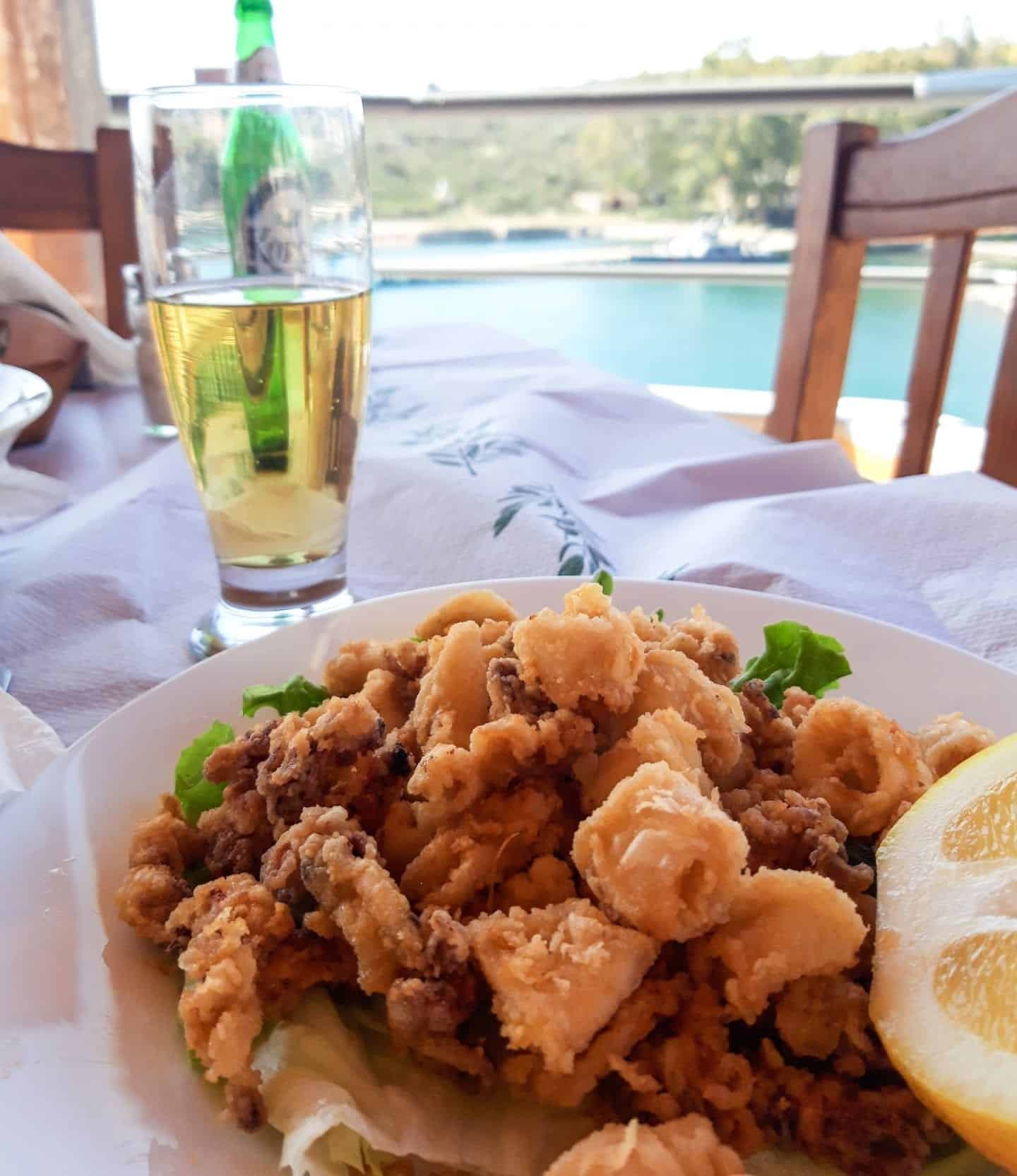Explore la famosa comida albanesa, lugar de calamares fritos con rodaja de limón junto a un vaso de cerveza sobre un mantel blanco