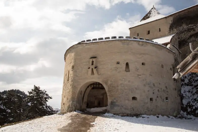 ¡Encuentra los 13 castillos más increíbles de Europa que debes ver! Entrada de la torre de piedra redonda con puerta arqueada y portcullis de metal elevado bajo una capa fresca de nieve blanca