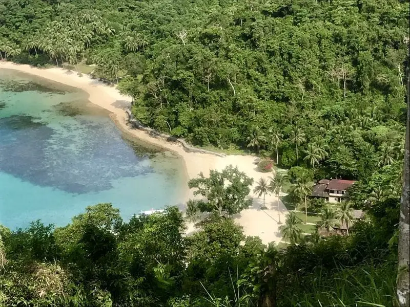 Explore las islas de Filipinas, hotel ubicado entre palmeras verdes en una playa de arena junto a una laguna rodeada de bosque