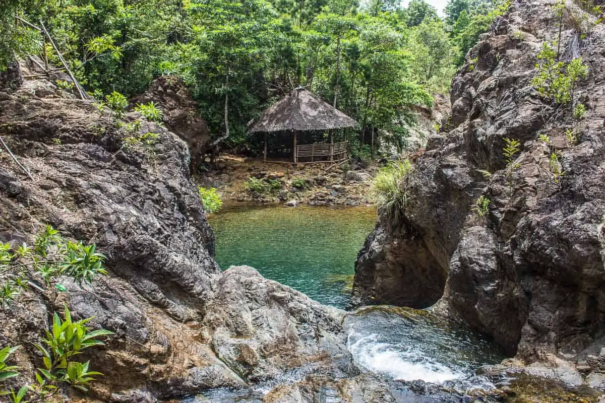 Las islas Filipinas más bellas, imagen de una cabaña de madera al aire libre entre acantilados rocosos con una cascada que desciende hacia una piscina cerrada