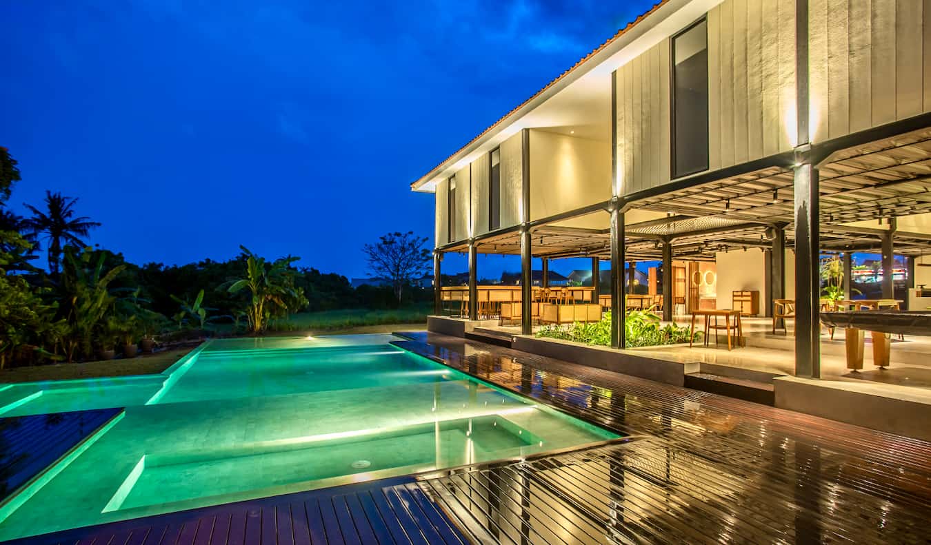 El exterior del albergue Tribal Bali por la noche con la piscina iluminada en primer plano