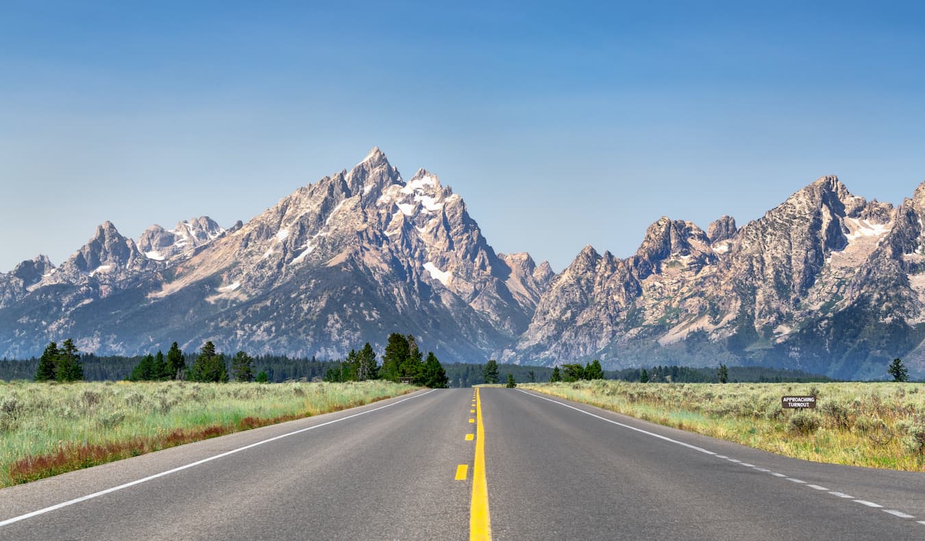 El camino abierto en un día soleado en Wyoming, EE. UU., con montañas al fondo