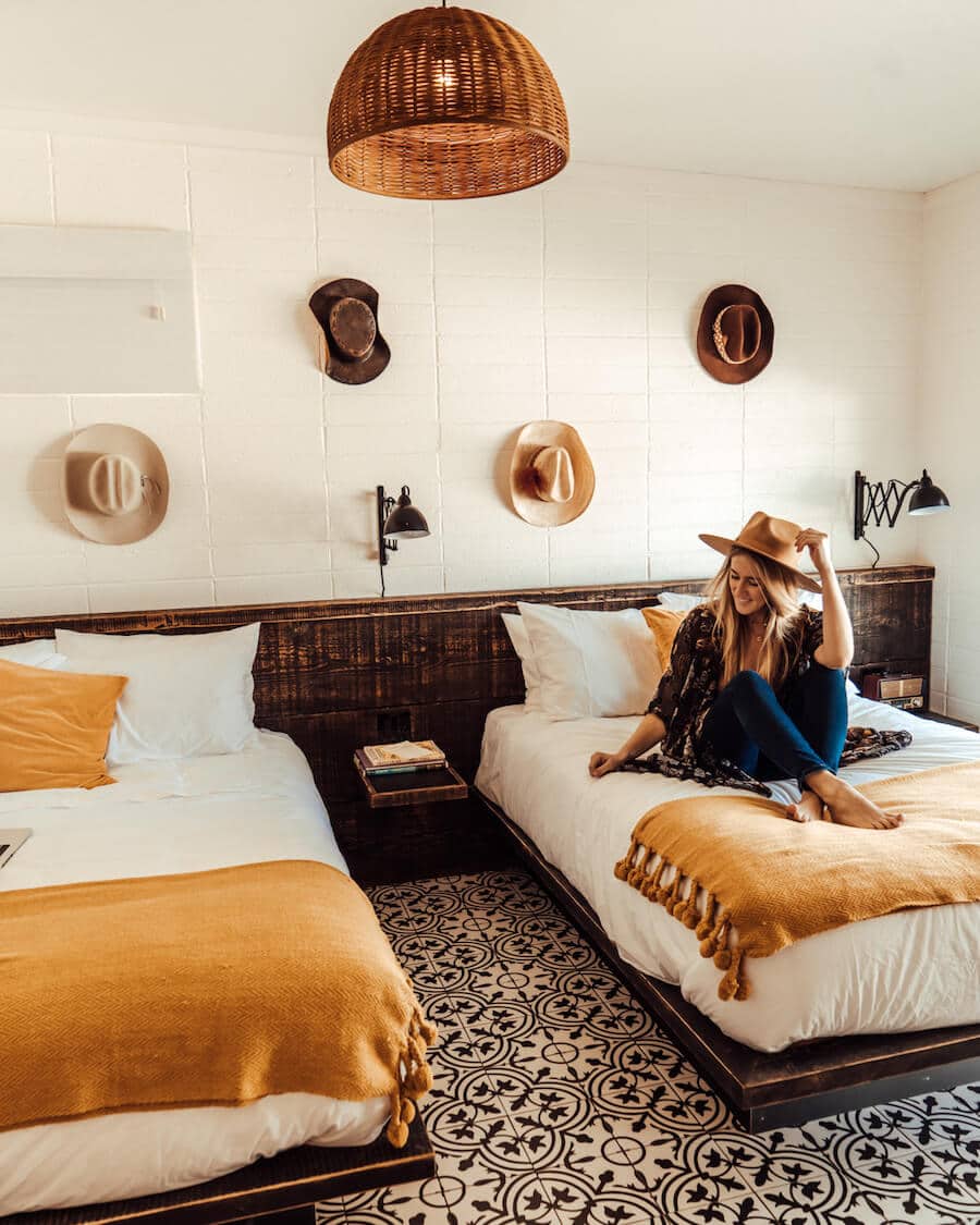 Interior de habitaciones en Cuyama Buckhorn con sombreros en la pared y una chica sentada en la cama